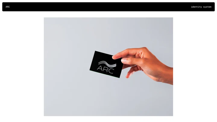 A hand holding a black ARC business card with the white wave mark